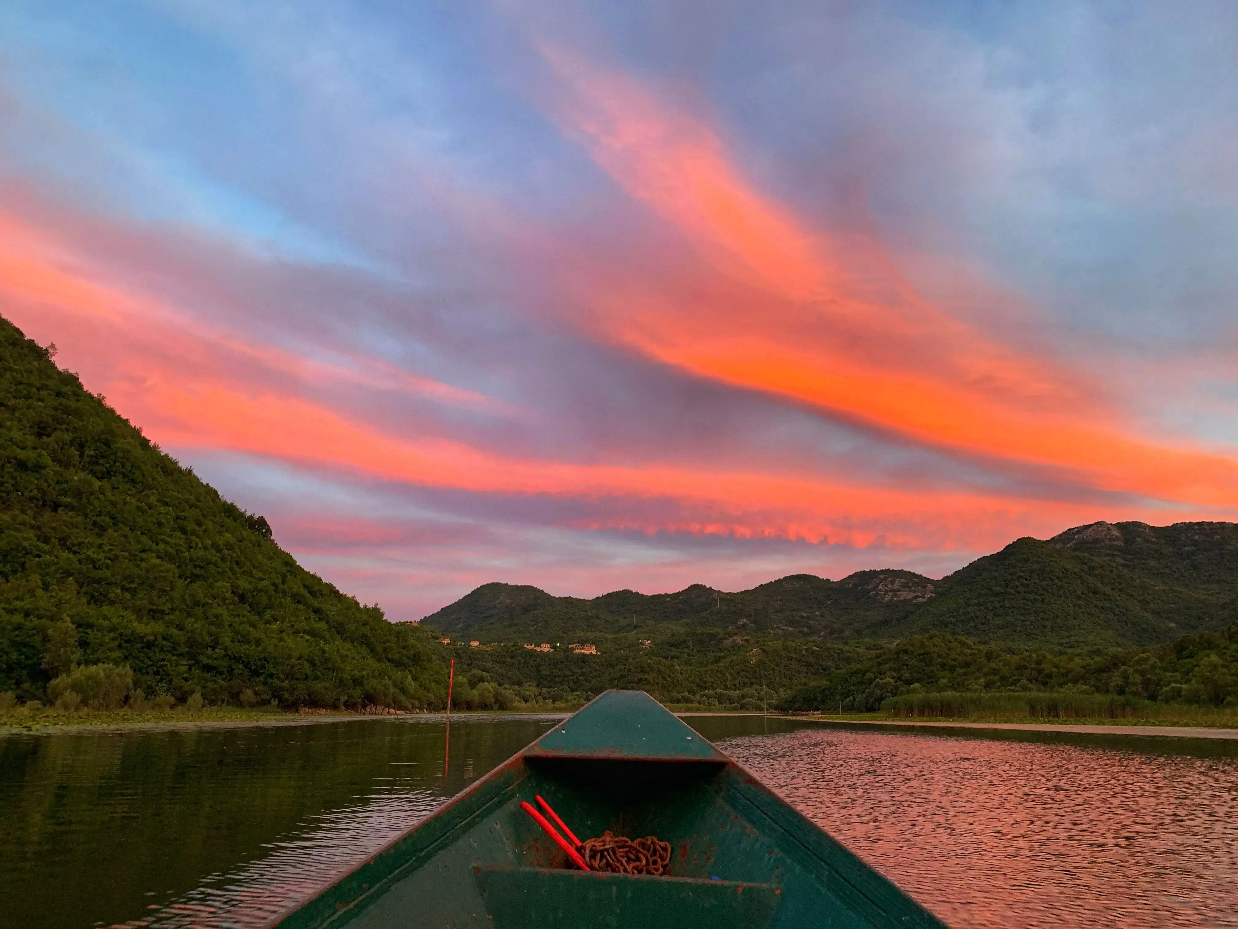 Wooden boat drifting across Skadar Lake at sunrise with mist over the water